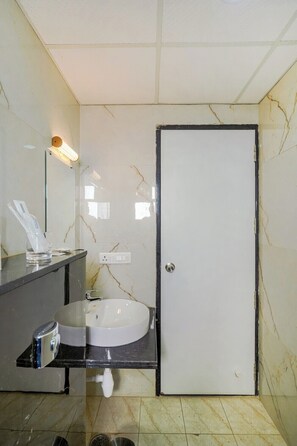 A bathroom with a white sink, a mirror, a towel dispenser, and a door. - Urban Suites by BluSalzz Rajasthan (Jaipur)