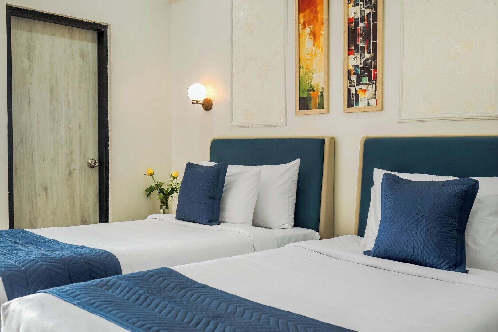 Ein Hotelzimmer mit zwei Betten, einem Nachttisch, einer Wandleuchte und zwei gerahmten Kunstwerken.