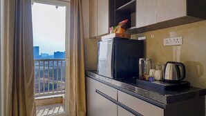 Una cocina moderna con un refrigerador negro, un microondas y una tetera sobre la encimera. Hay una ventana con cortinas, y se ve un balcón afuera.