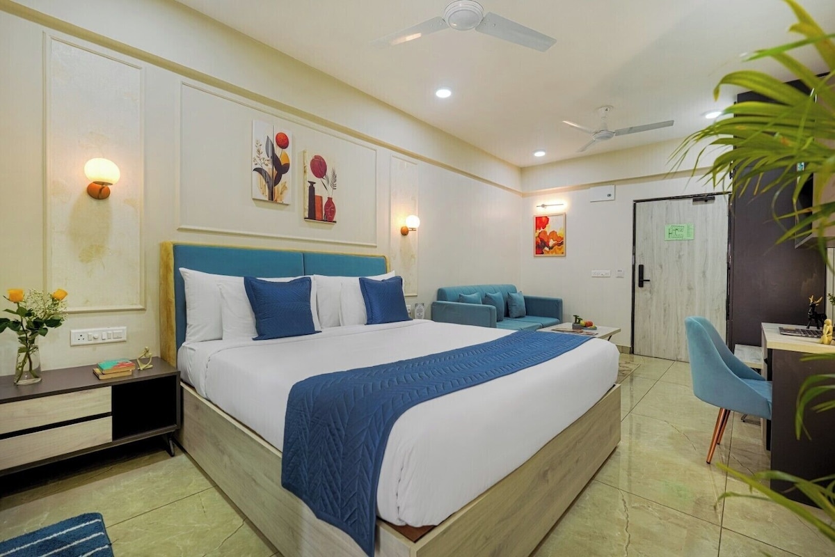 A hotel room with a bed, bedside table, desk, chair, and a door.