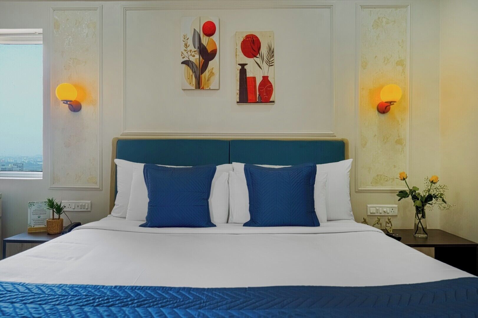 A hotel room with a large bed, two wall-mounted lamps, and two paintings on the wall.