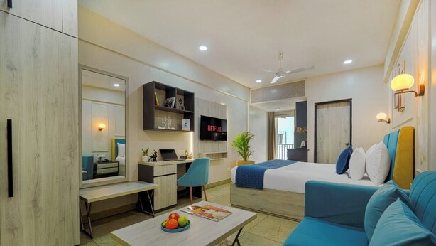 Una habitación de hotel moderna con cama, escritorio, sofá, televisión y planta.