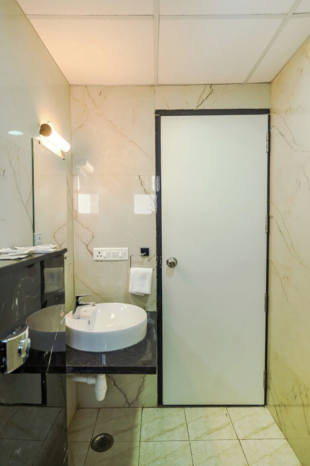 Une salle de bain avec un lavabo blanc, un miroir, un porte-serviettes et une porte.