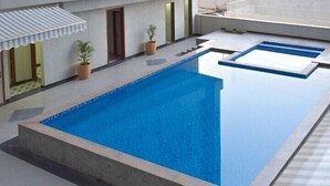 Piscina rectangular con solárium empedrado, plantas en macetas y un área de estar cubierta.