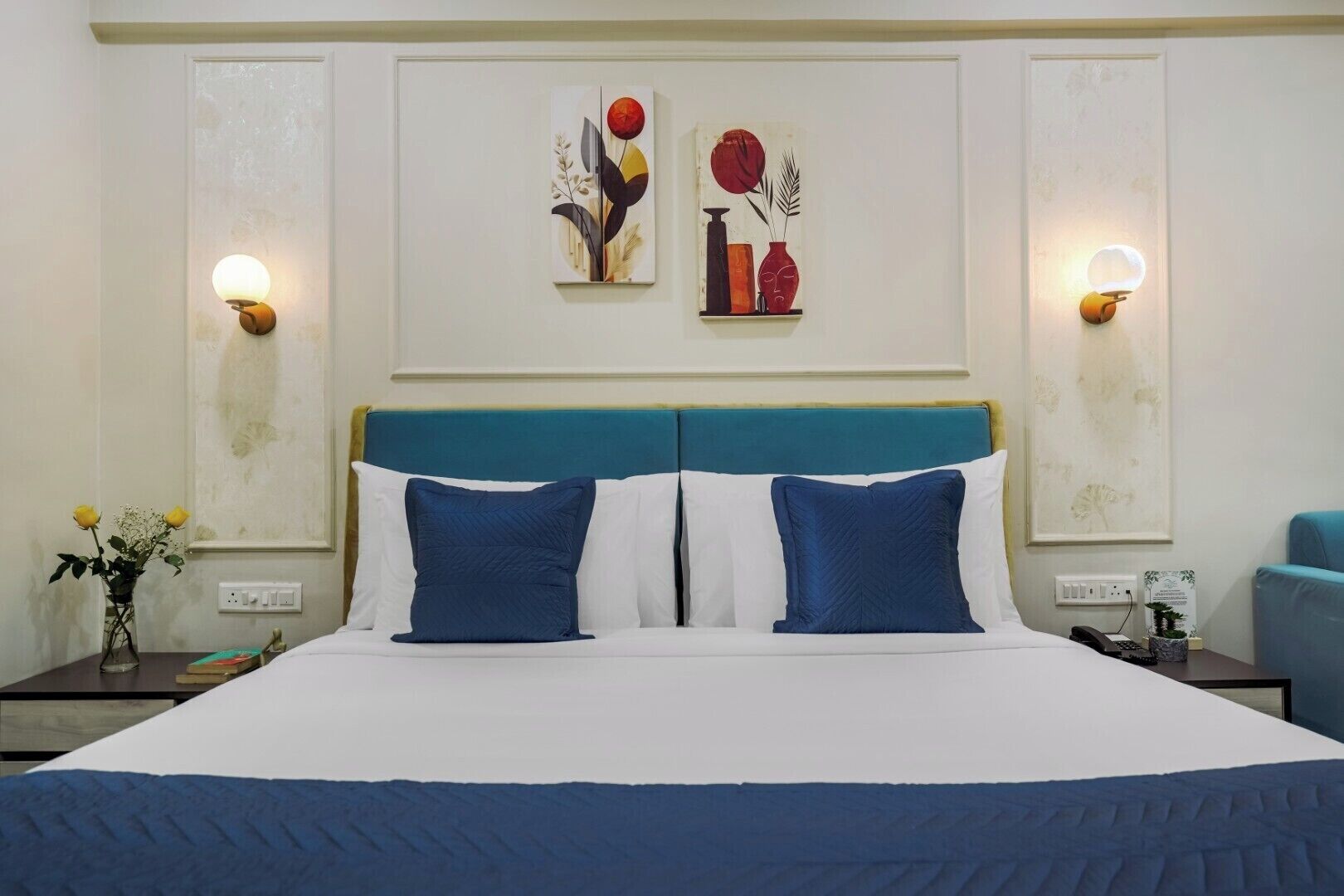 A double bed with a teal headboard, two blue pillows, and a white bedspread. There are two wall-mounted light fixtures on either side of the bed.