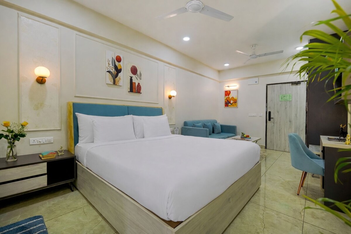 A hotel room with a large bed, a desk, a blue sofa, and a ceiling fan.