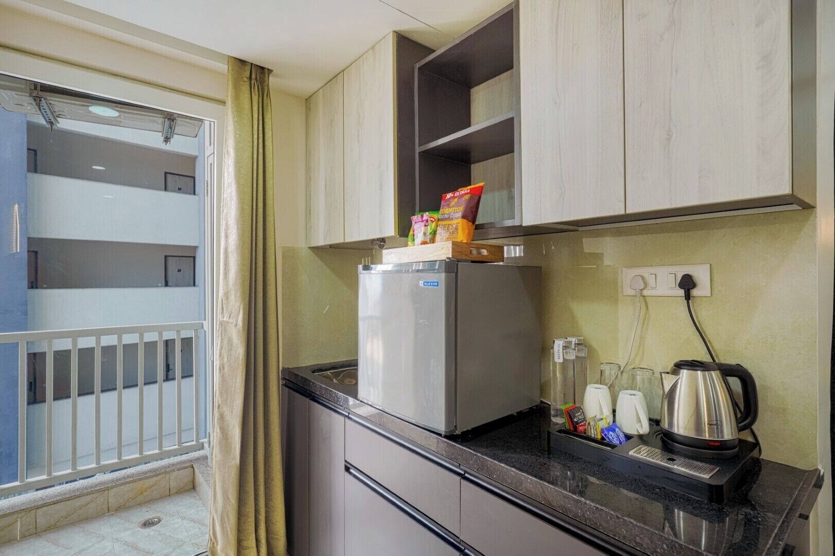 A compact kitchen with a refrigerator, a kettle, and a coffee maker on the counter.