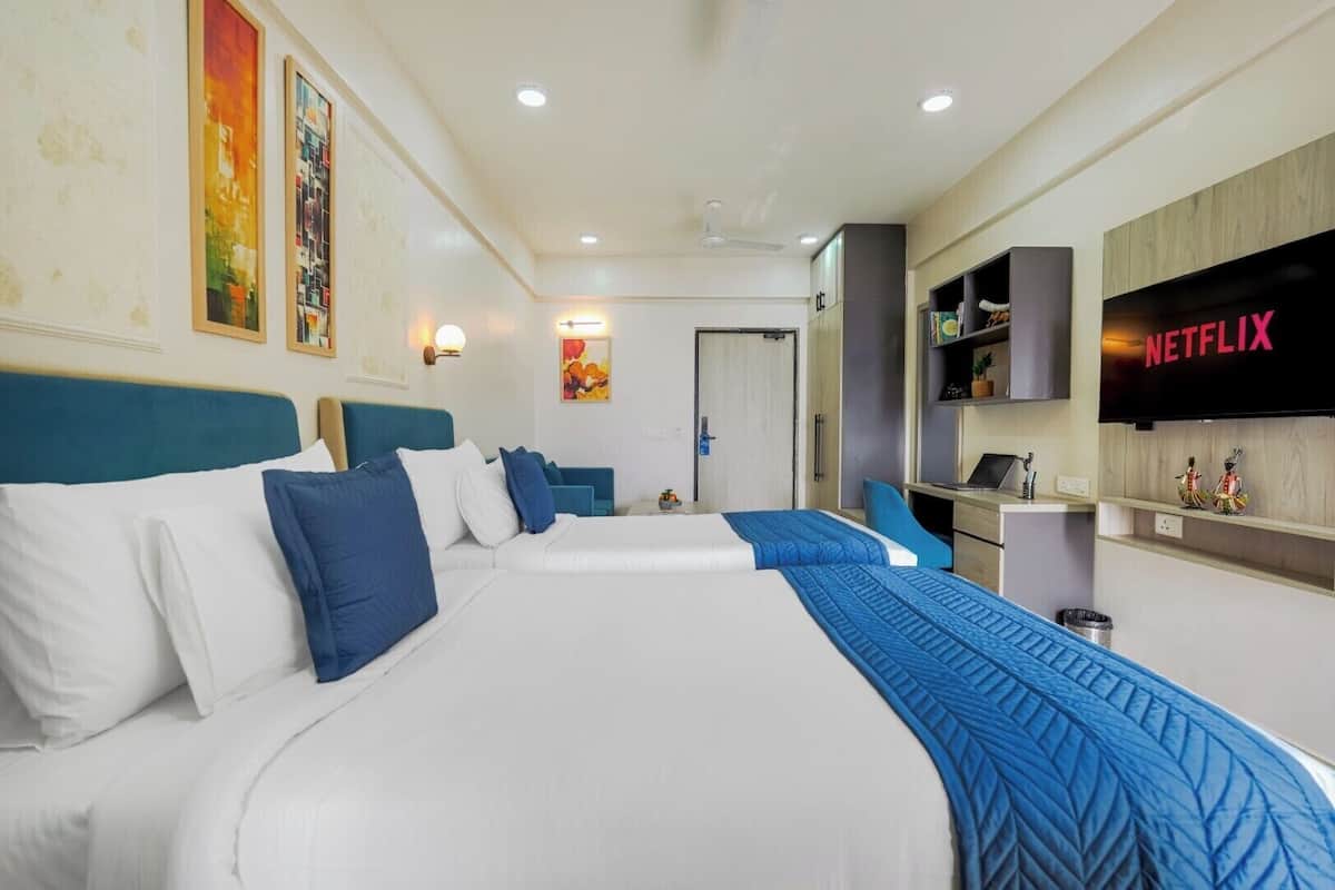 A hotel room with two beds, a desk, a chair, a TV, and artwork on the walls.