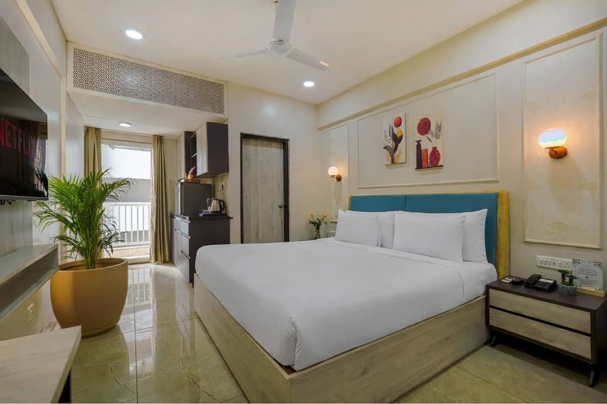 A hotel room with a bed, bedside table, TV, potted plant, and a view of the balcony.