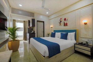 A hotel room with a bed, bedside table, TV, potted plant, and a view of the outside. - Urban Suites by BluSalzz Rajasthan (Jaipur)