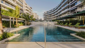Una piscina con sillones de descanso y un edificio moderno con balcones.