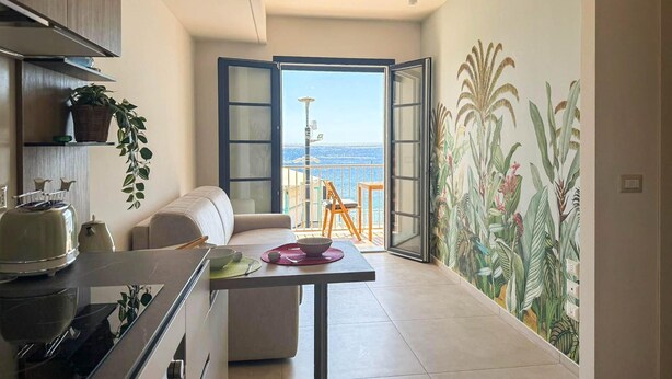 Une cuisine moderne avec un coin repas, un canapé et une vue sur la mer, visible à travers une porte ouverte.