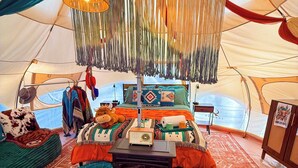 A cozy interior with a bed, a table with a radio, and hanging lamps. - Pasture Bedtime Yurt (Middleburg)