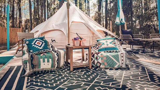 A tent with a table and chairs, surrounded by patterned rugs and a wooden deck. - Pasture Bedtime Yurt (Middleburg)