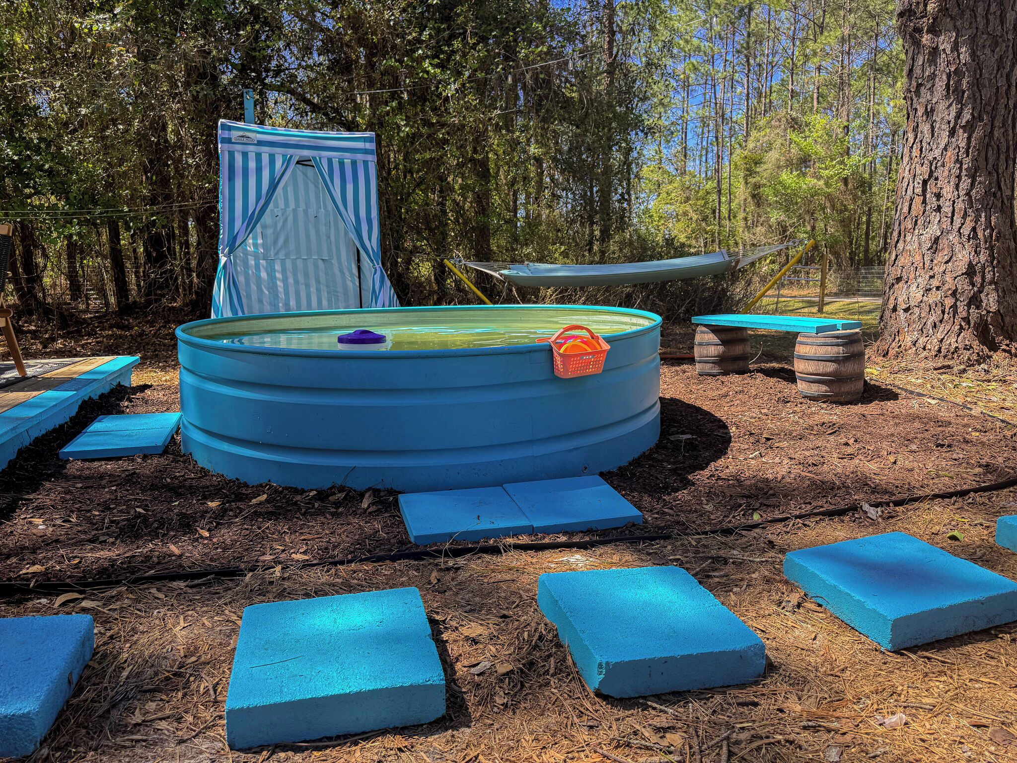 Une piscine circulaire recouverte d’une bâche bleue, avec un petit panier orange à proximité.
