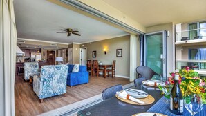 Een ruime zithoek met een blauwe bank, een eettafel gedekt voor twee personen, en een balkon met uitzicht.