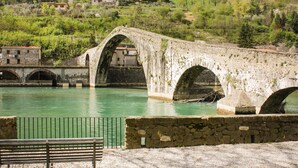 Un pont de pierre enjambe une rivière, et un banc est visible au premier plan.