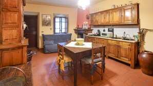 Une cuisine chaleureuse avec des meubles de rangement en bois, une table à manger avec des chaises, un canapé bleu et un luminaire suspendu.