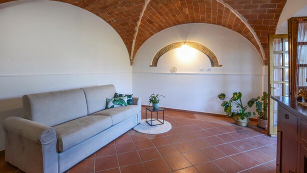 A living room with a sofa, a round table, and potted plants. - Appartamento Casale Le Risaie (Vicopisano)