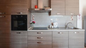 A modern kitchen with a built-in oven, a stainless steel sink, and wooden cabinetry. - Appartamento Casale Le Risaie (Vicopisano)