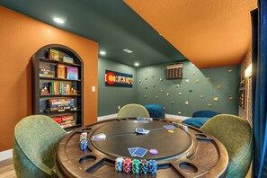 Ein Raum mit einem Pokertisch, Stühlen, einem Bücherregal und Wandgriffen.