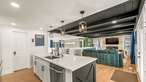 Cozinha moderna com ilha central, área de jantar com sofá verde e sala de estar com lareira.
