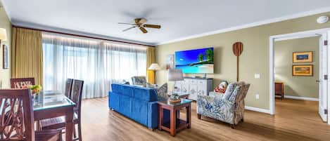 Una sala de estar con una mesa de comedor, un sofá azul, un sillón estampado y un televisor.