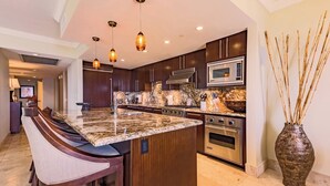 Una cocina moderna con armarios de madera oscura, encimera de granito, electrodomésticos de acero inoxidable e iluminación colgante.