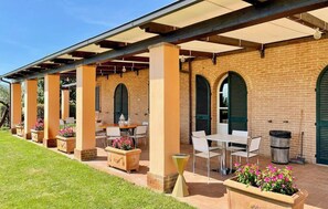 Eine Terrasse im Freien mit Ziegelmauern, grünen Fensterläden und weißen Tischen und Stühlen.