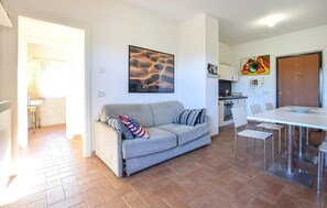 Ein Wohnzimmer mit einer Couch, einem Esstisch mit Stühlen, einer Küchenzeile und einer Tür.