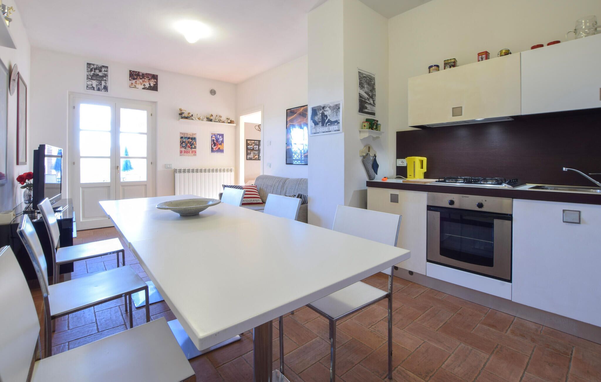 Une cuisine moderne avec des meubles blancs, une table à manger et des chaises. Elle est équipée d’un four encastré et d’une cuisinière.