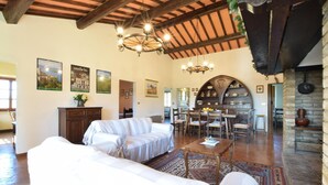 A spacious living area with a high ceiling, a dining area with a large wooden table, and a kitchen with a brick wall and wooden beams. - Umbria Magione Podere C. (Magione)