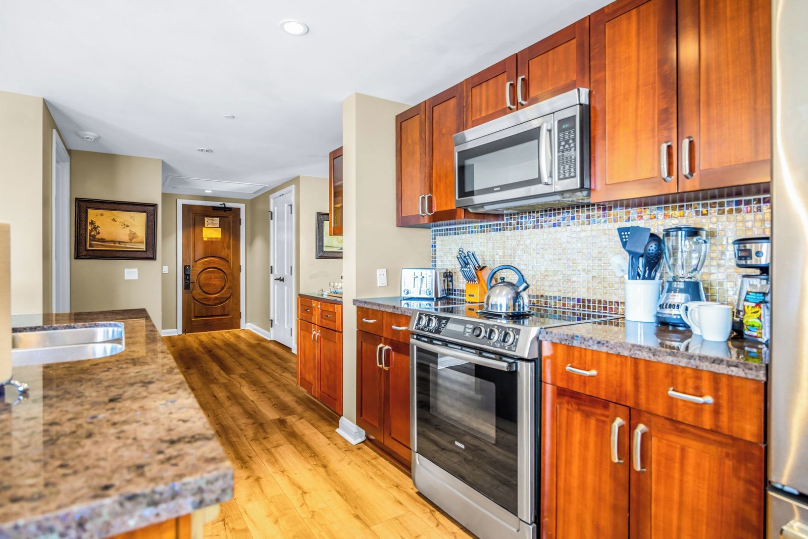 A kitchen with wooden cabinets, a stainless steel microwave, a stove, and a tiled backsplash.
