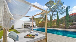 Un pontile in legno con un letto, una piscina e una casa moderna sullo sfondo.