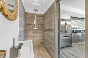 A modern bathroom with a shower, a large mirror, and a kitchen area with stainless steel appliances. - Maison de l’Esterel 5 BR - Private Pool, Frejus, France (Frejus)