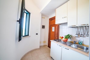 Cozinha compacta com armários brancos, pia de aço inoxidável e janela com moldura preta.