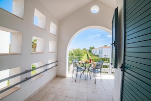 Ein Balkon mit Tisch und Stühlen, Blick auf einen Garten und ein Gebäude im Hintergrund.