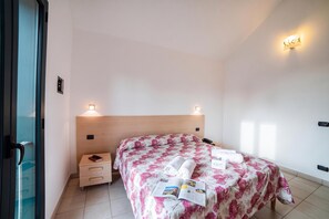 Hotellihuone, jossa on puinen pääty, kukallinen vuodevaatteisto, yöpöytä, jossa on kirja ja puhelin, sekä kaksi seinälle asennettua valaisinta.