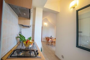 A kitchen with a gas stove, a bowl of vegetables, and a dining area with a table and chairs. - Beach in 5 min | Pool Access | n.66, Otranto, Italy (Otranto)