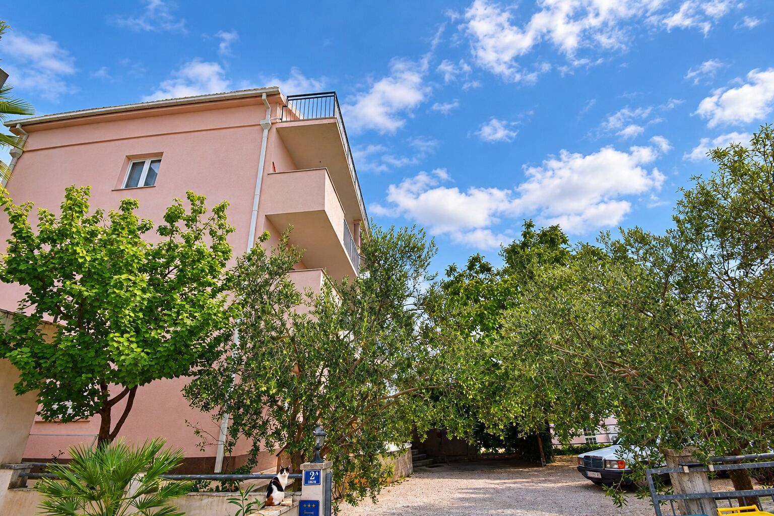 A pink building with a balcony, surrounded by trees and a clear sky.