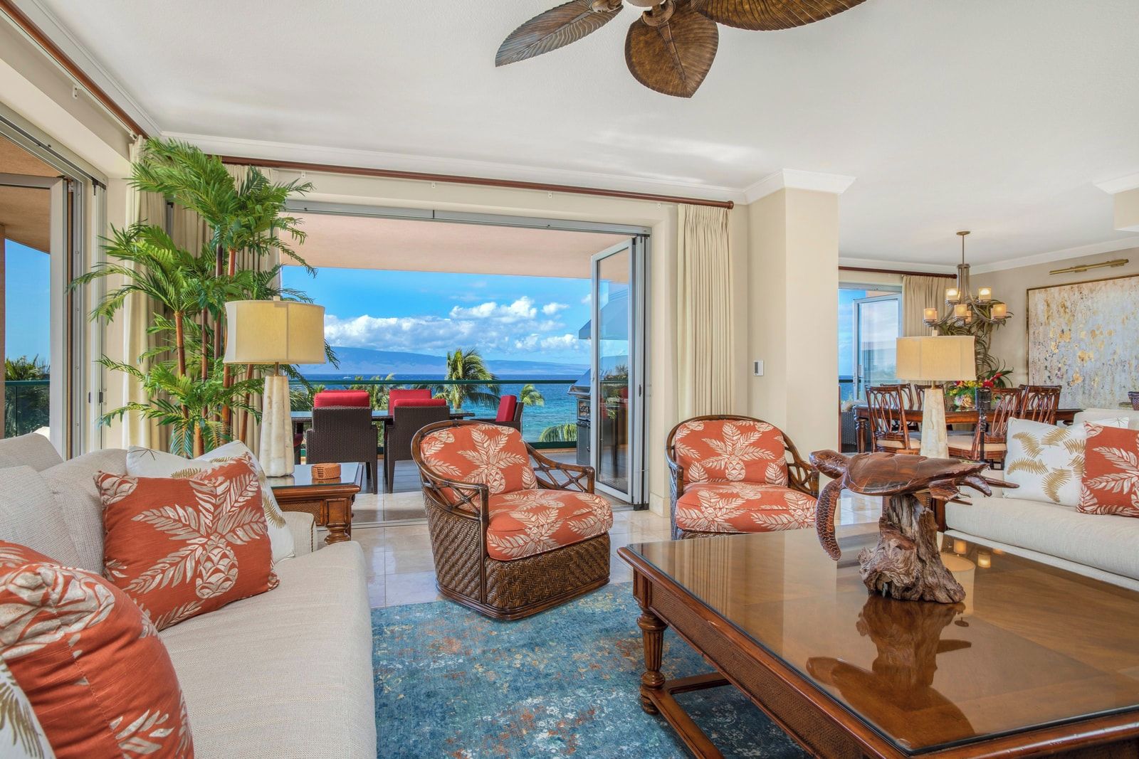 Een ruime woonkamer met balkon en uitzicht op de oceaan, ingericht met een bank, stoelen en een salontafel.