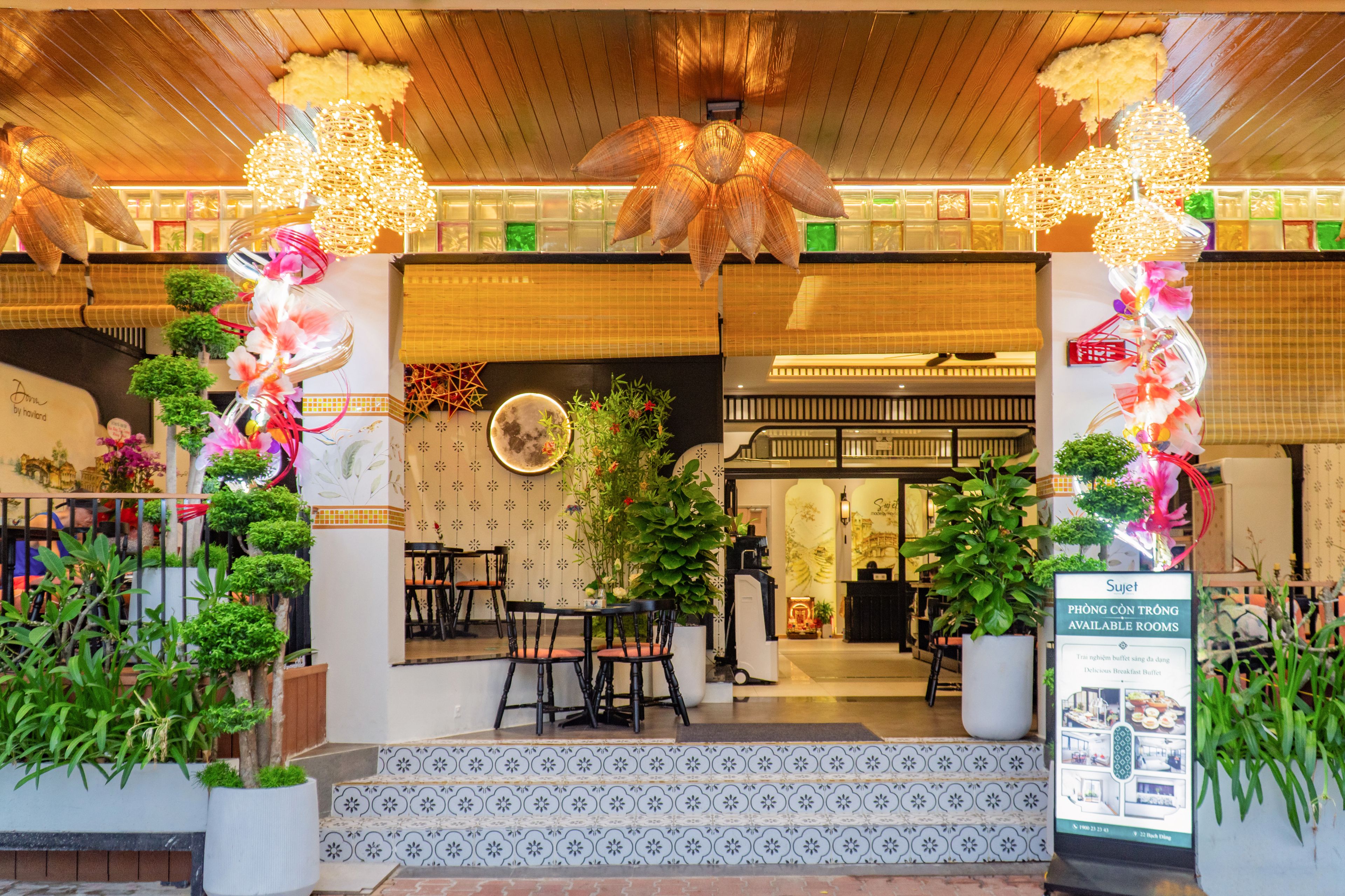 A hotel entrance with a traditional Asian architectural style, featuring a wooden ceiling, decorative hanging lights, and potted plants.