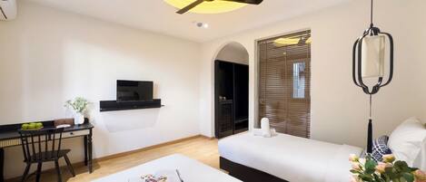 Habitación de hotel con cama, escritorio con televisor, ventilador de techo y ventana con persianas.