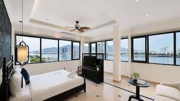 A modern hotel room with a bed, a TV, a desk, and large windows offering a city view.