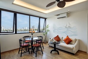 Un salon moderne avec vue sur la ville, un coin repas avec des chaises, un canapé avec des coussins et un mur orné d’une fresque aux motifs maritimes.