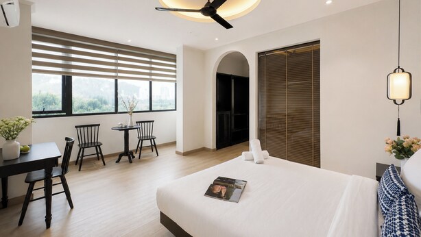 A modern hotel room with a large bed, a dining area with a table and chairs, a ceiling fan, and large windows with blinds. - Sujet Marina Da Nang Hotel by Haviland (Da Nang)