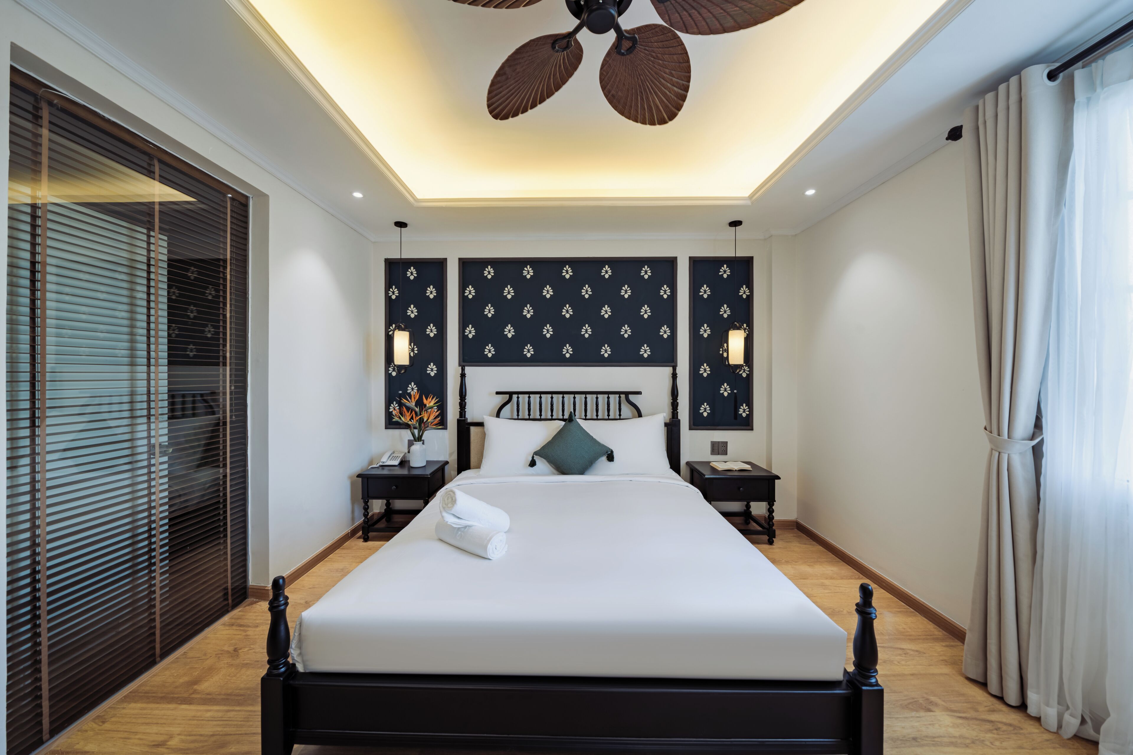 Habitación de hotel moderna con una cama grande, dos mesitas de noche, un ventilador de techo y vistas a la ciudad.