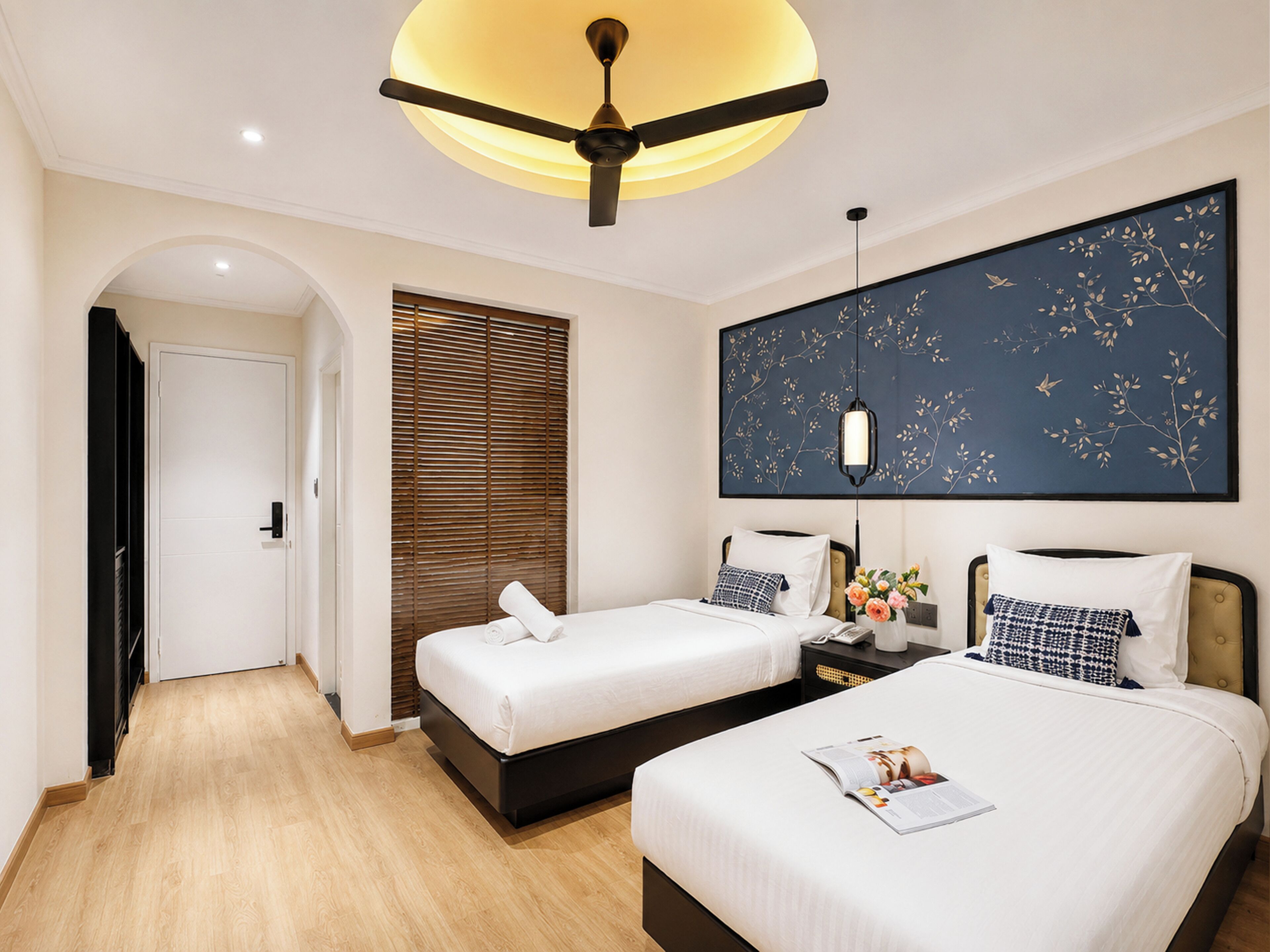 A hotel room with two beds, a ceiling fan, a wall-mounted artwork, and a wooden floor.