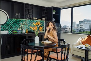 A modern kitchen with a green tiled backsplash, a dining area with a round table and chairs, and a view of the city through large windows. - Sujet Marina Hotel Da Nang By Haviland (Da Nang)