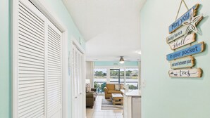 A hallway with a view to a dining area, a kitchen, and a window with blinds.